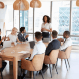 A confident nonprofit leader stands to present in a boardroom filled with diverse professionals, symbolizing strategic planning, collaboration, and forward-thinking fundraising practices.