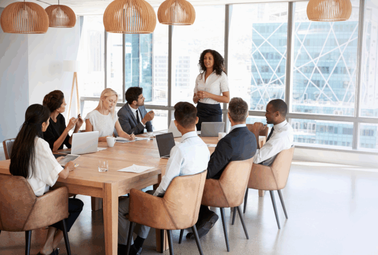 A confident nonprofit leader stands to present in a boardroom filled with diverse professionals, symbolizing strategic planning, collaboration, and forward-thinking fundraising practices.