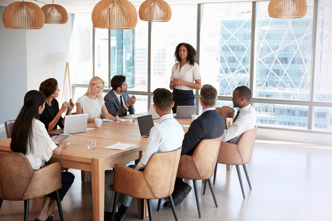 A confident nonprofit leader stands to present in a boardroom filled with diverse professionals, symbolizing strategic planning, collaboration, and forward-thinking fundraising practices.
